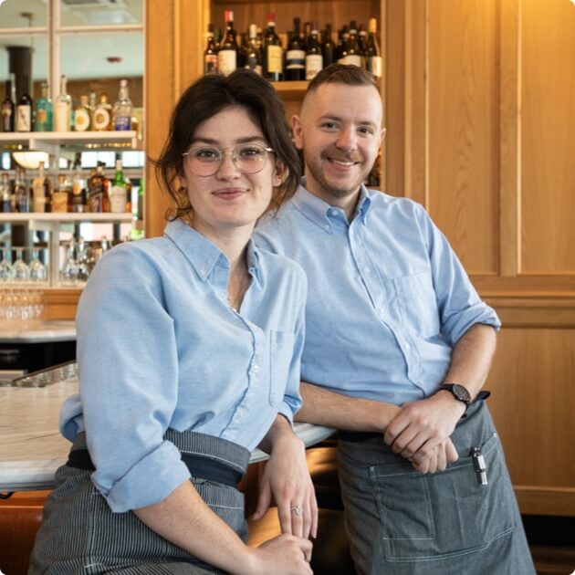 Two people smiling in front of a restaurant bar