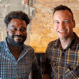 Two people smiling in front of a brick wall